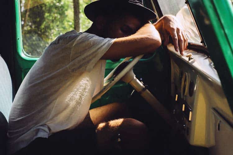 young man asleep at wheel in car