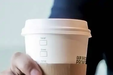 man holding paper cup of coffee with plastic lid