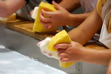 hands of young children cleaning with sponges and soapy water