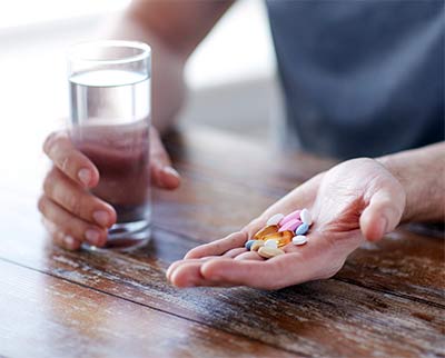 man with handful of supplements and water glass