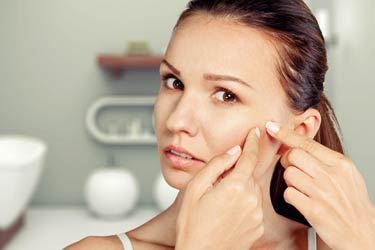 woman touching pimple blemish in mirror